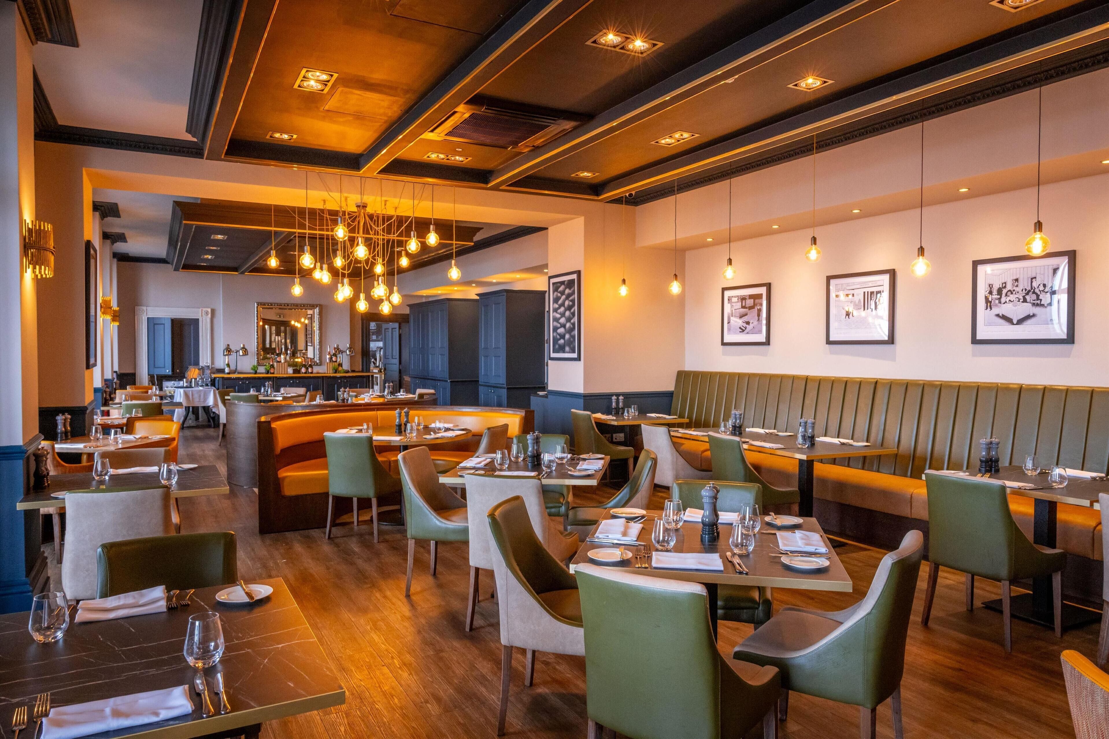 A restaurant with booths and tables, hanging light fixtures, and framed pictures on the walls.
