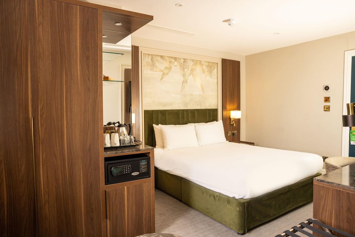 A hotel room with a bed, a desk, a mirror, and a wall-mounted artwork.