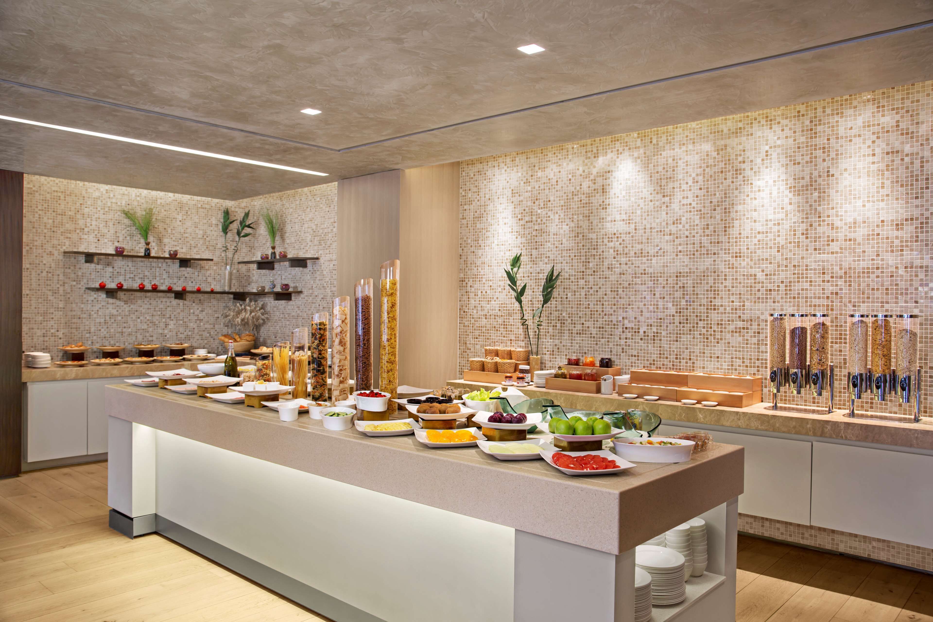 A buffet setup with various food items and beverages, a tiled wall, and shelves with decorative items.