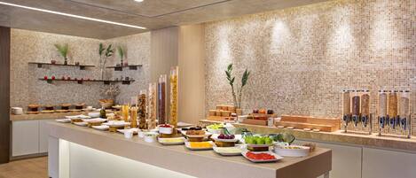 A buffet setup with various food items and beverages, a tiled wall, and shelves with decorative items.