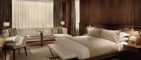 A modern hotel room with a large bed, a sofa, a coffee table, and a desk.