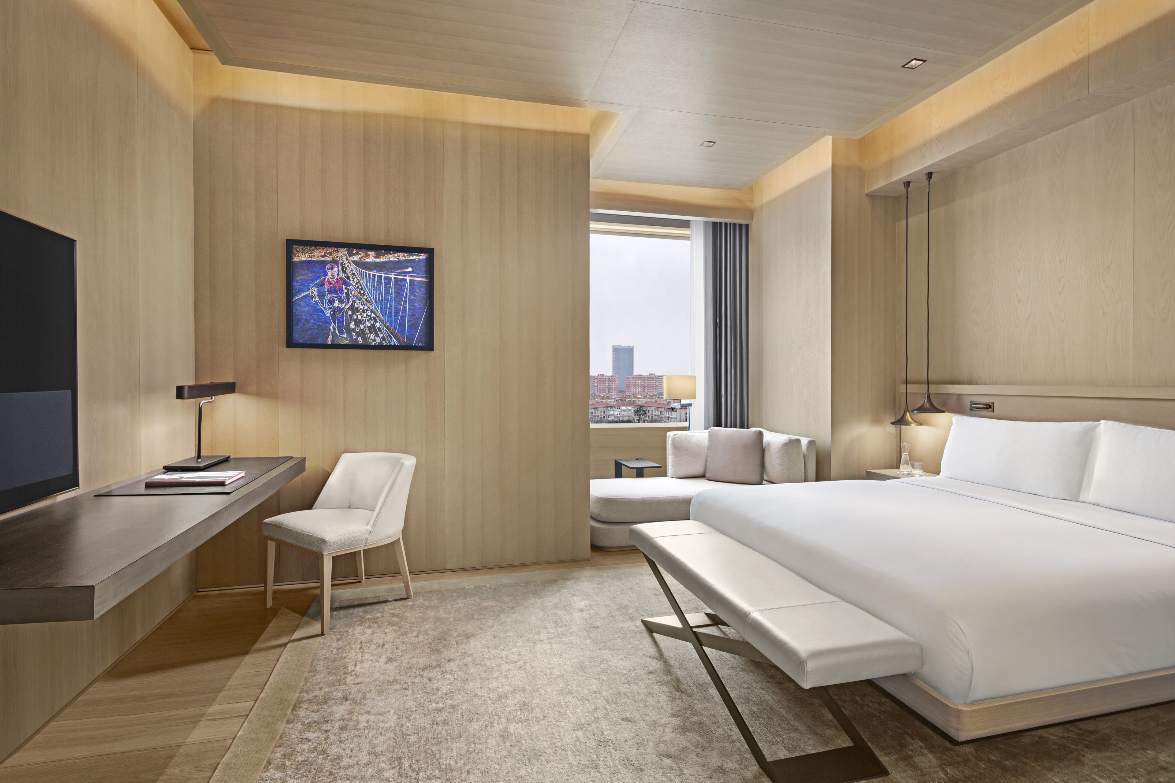 Una habitación de hotel moderna con una cama grande, un escritorio, una silla, un sofá y un televisor en la pared.