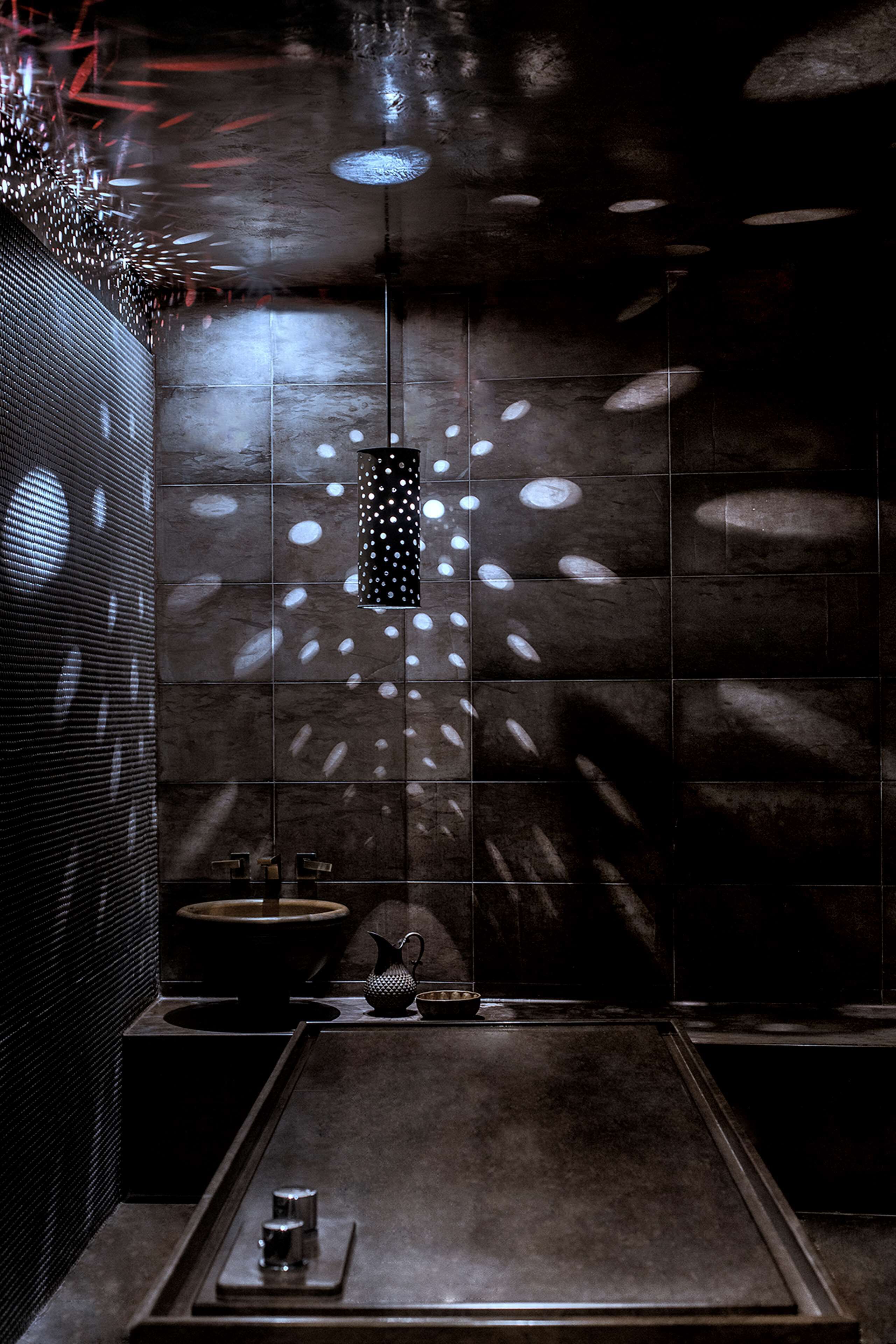 A modern bathroom with a dark tiled wall, a central sink, and a small mirror.