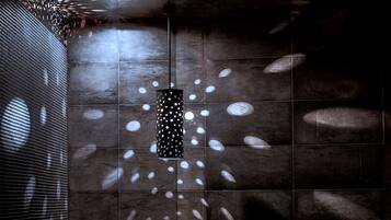 A modern bathroom with a dark tiled wall, a central sink, and a small mirror.