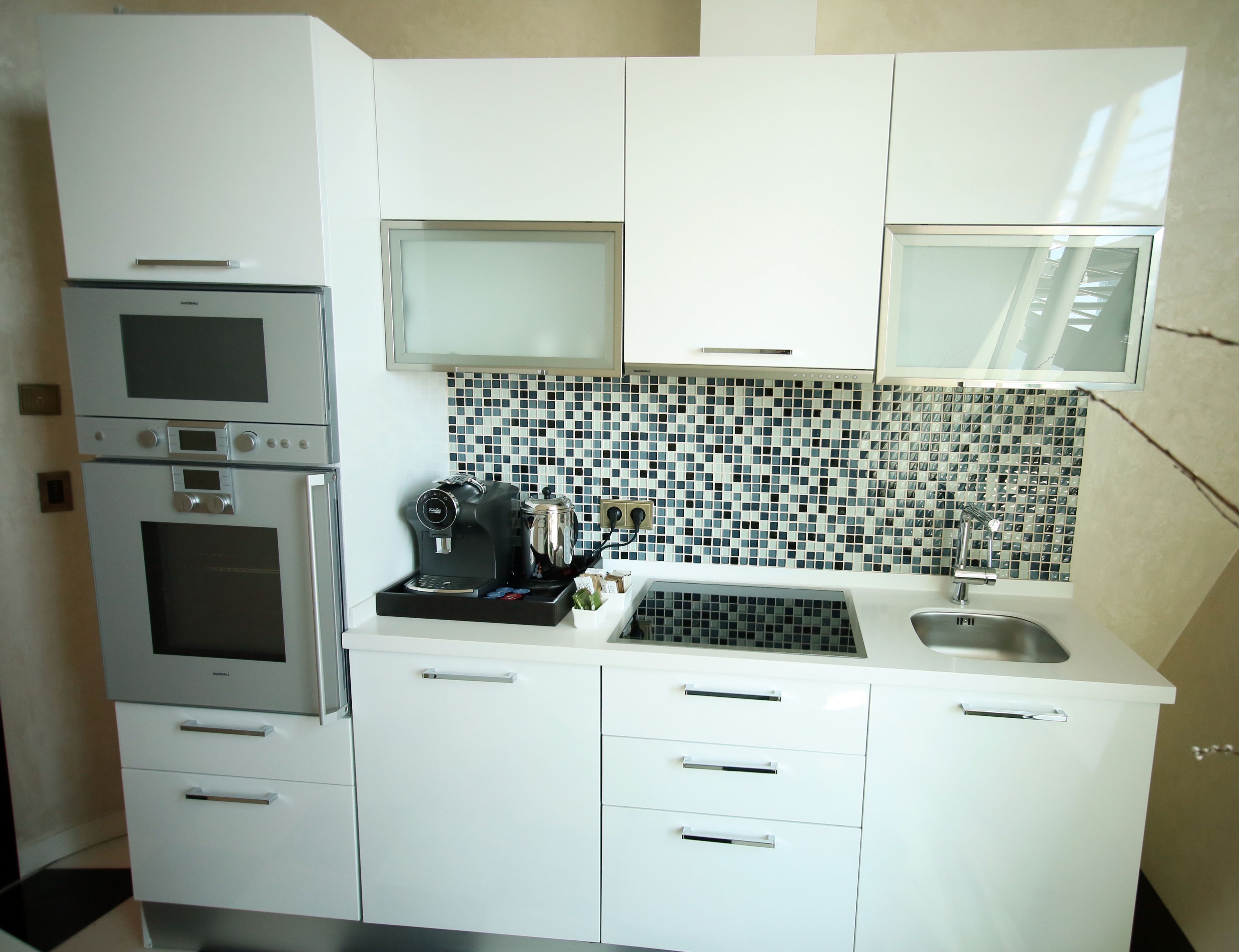 A modern kitchen with white cabinets, a built-in oven, a coffee maker, and a tiled backsplash.