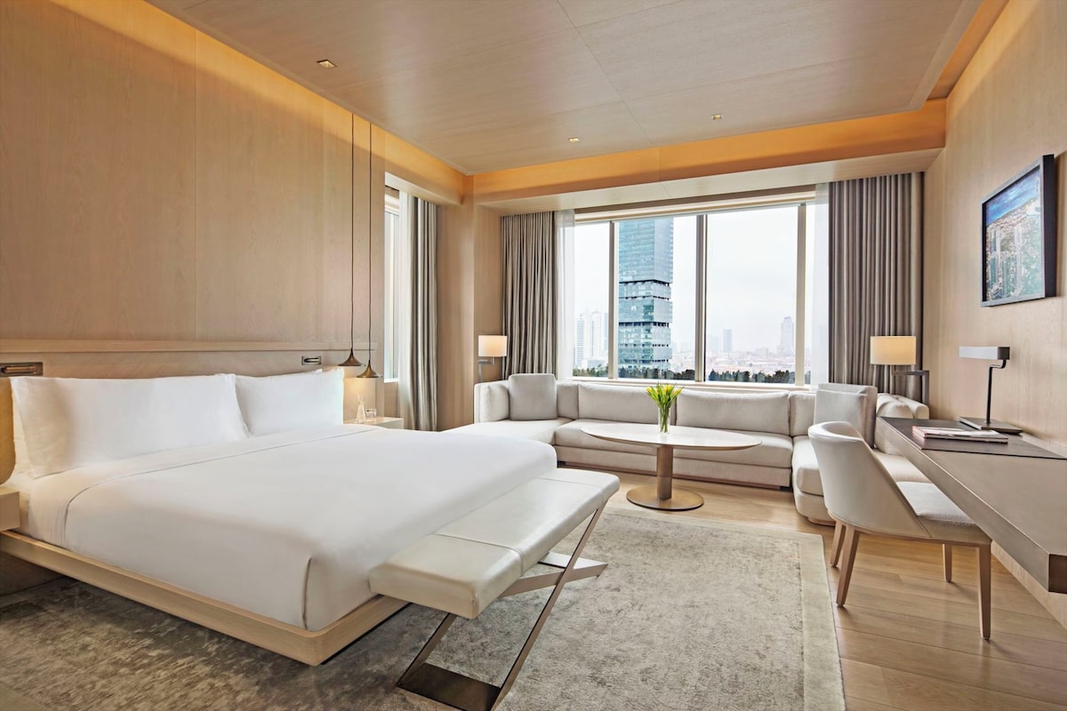 Habitación de hotel moderna con una cama grande, un sofá, un escritorio y vistas a la ciudad.