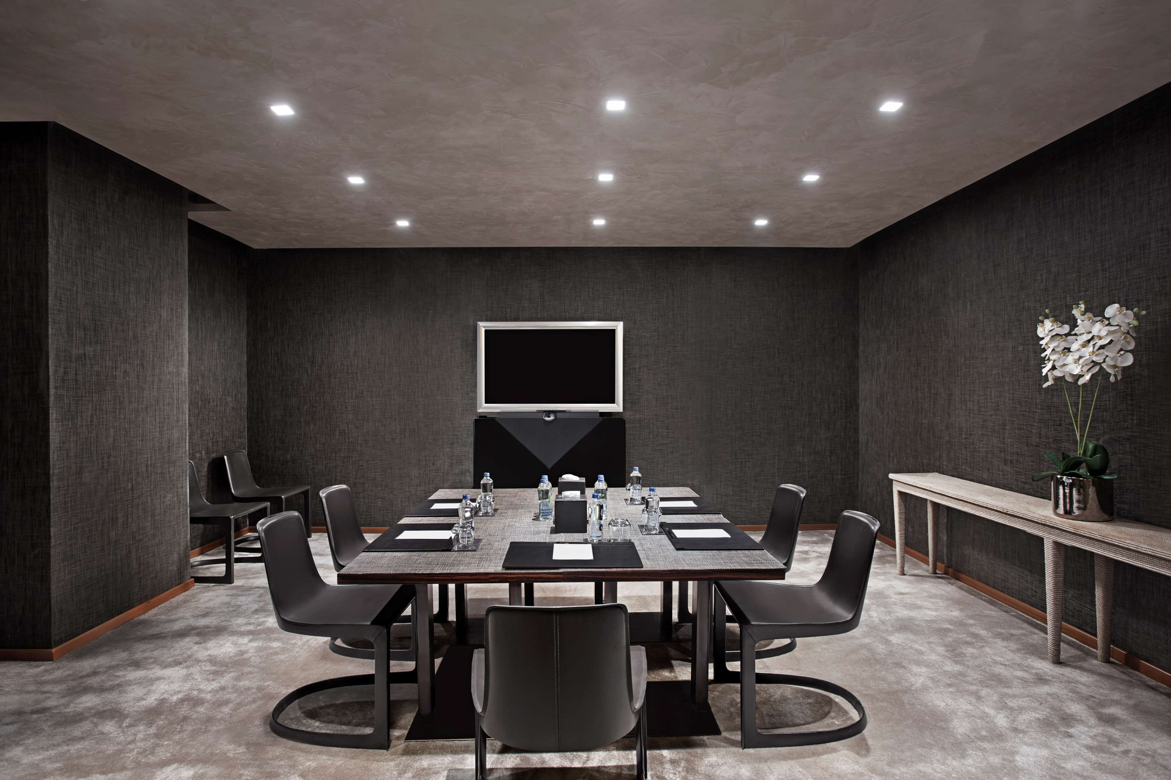 A conference room with a large table, chairs, a flat-screen TV, and a potted plant.
