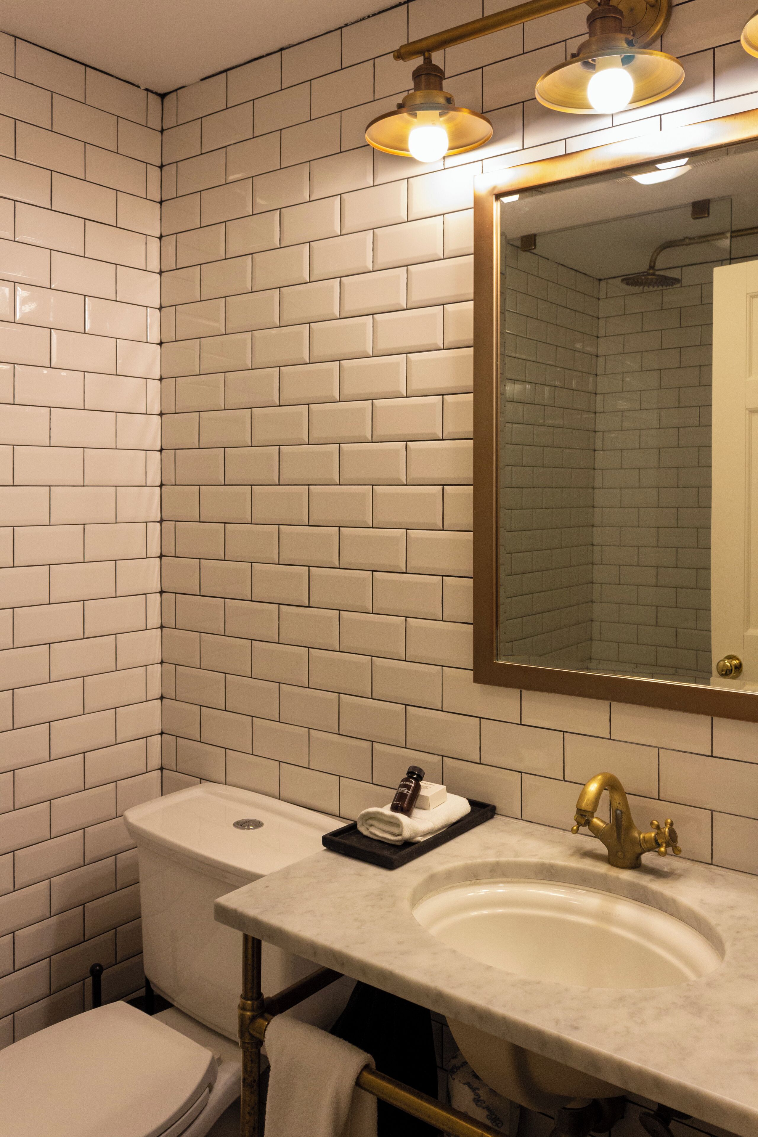 A bathroom with white subway tiles, a white sink with a gold faucet, and a mirror with a gold frame.