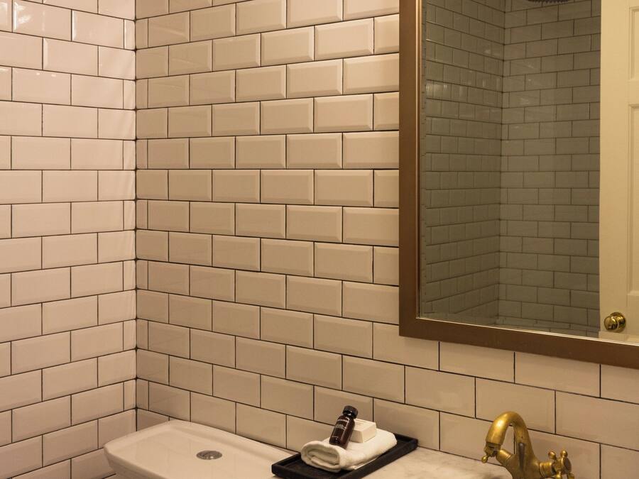 A bathroom with white subway tiles, a white sink with a gold faucet, and a mirror with a gold frame.