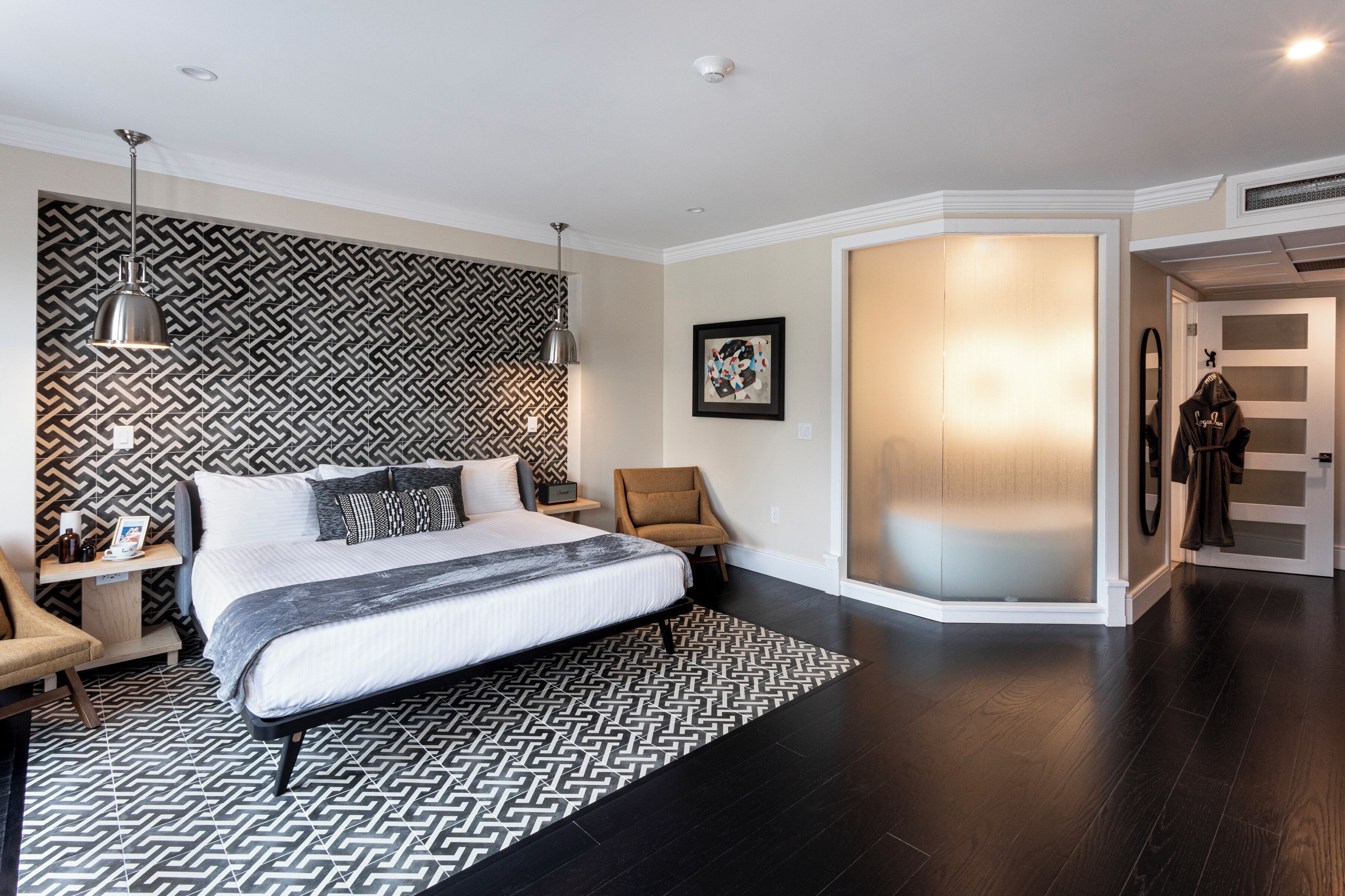 A modern bedroom with a large bed, a patterned rug, a chair, and a wardrobe.
