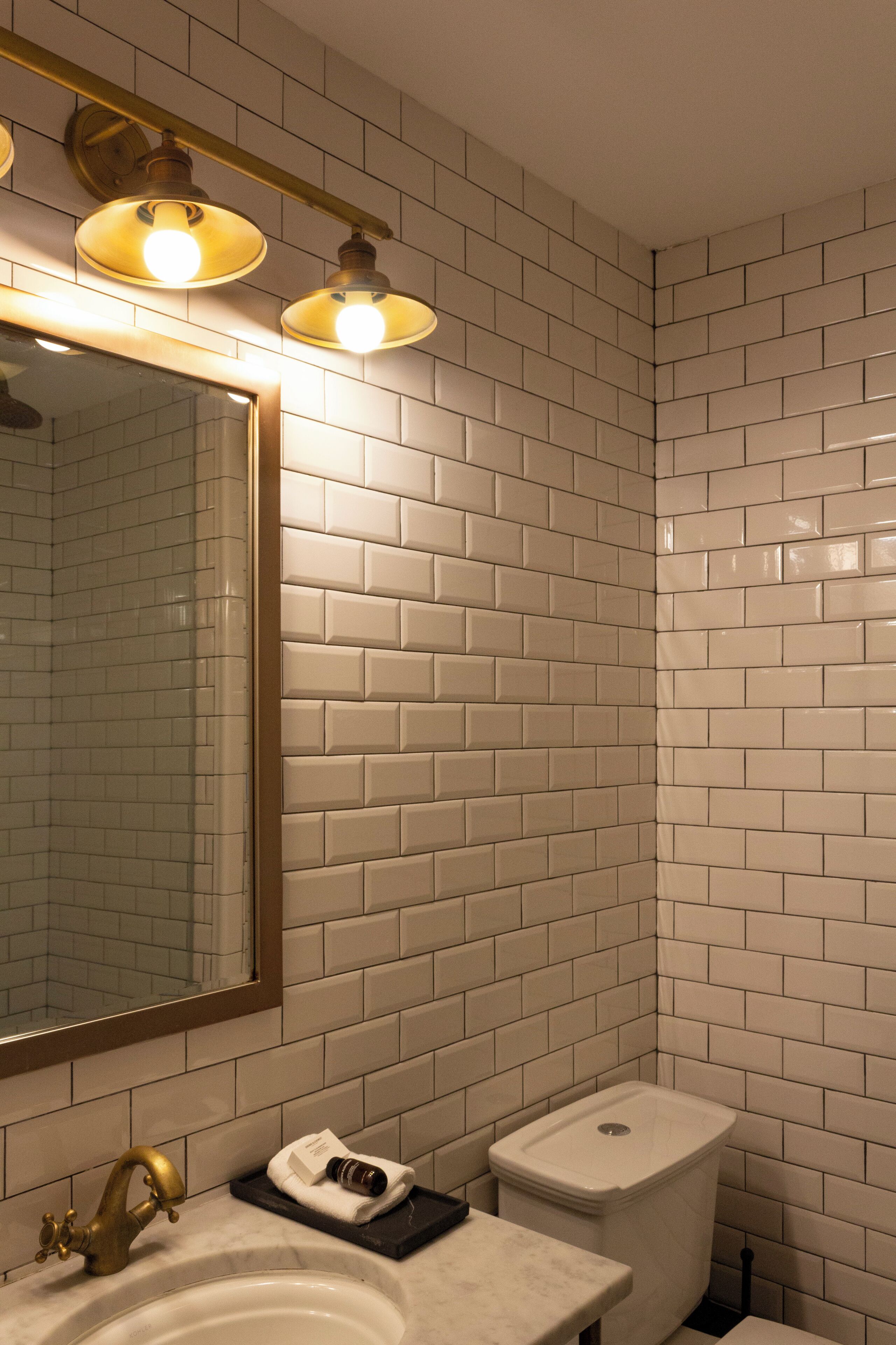 A bathroom with white subway tiles, a gold faucet, and a mirror with a gold frame.