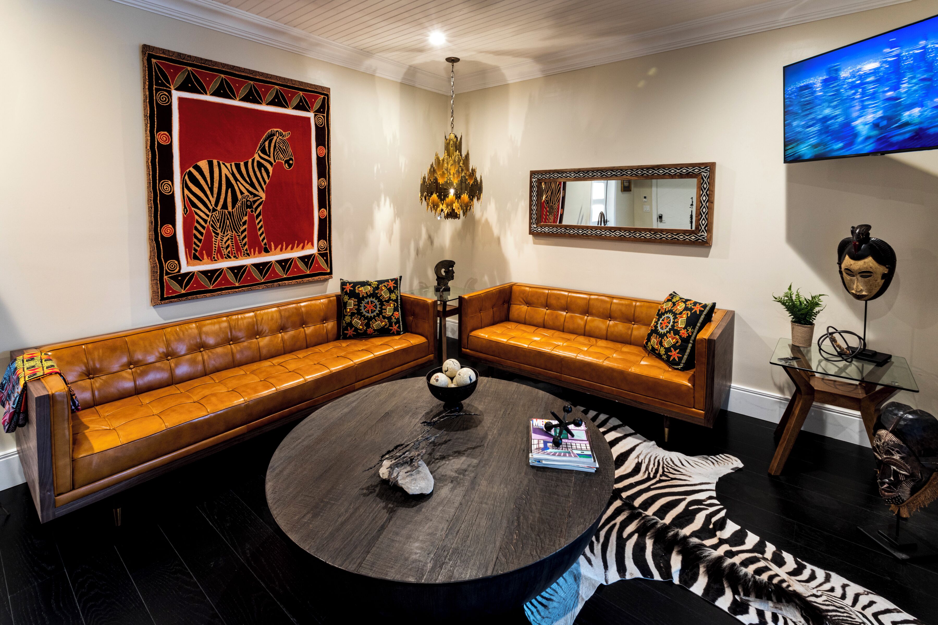 A living room with a brown leather sofa, a round coffee table, a zebra rug, and a large zebra painting on the wall.