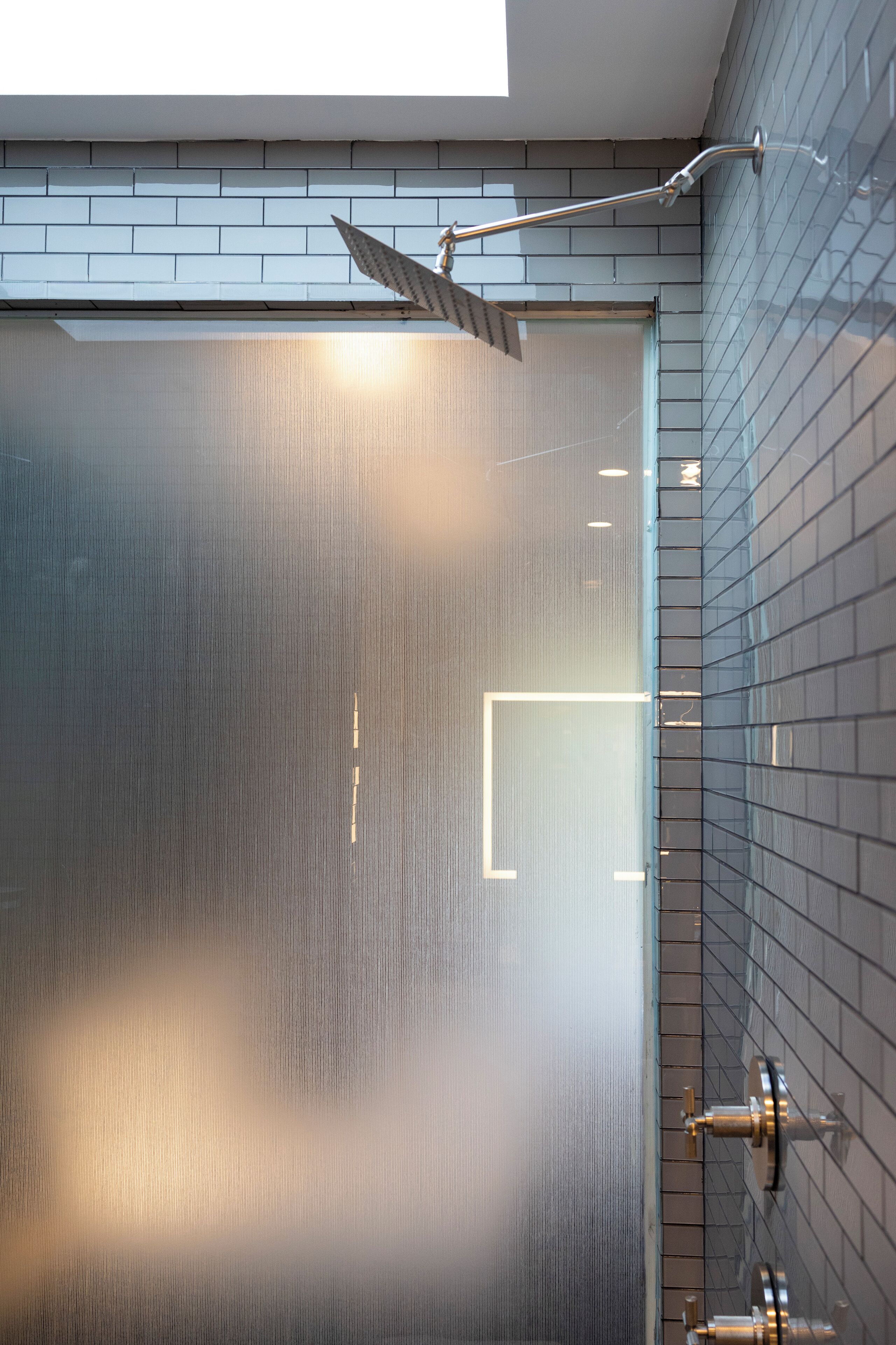 Une salle de bain moderne avec une douche à parois de verre, une pomme de douche visible et un mur carrelé.