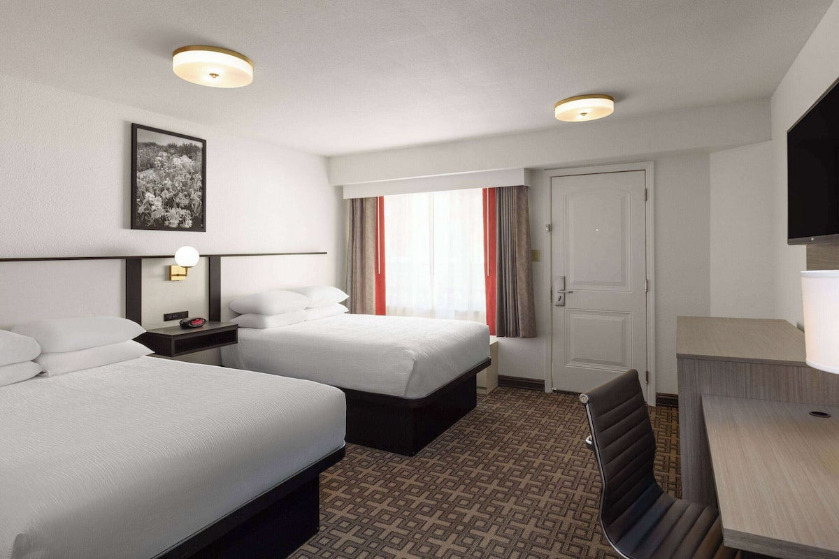 A hotel room with two beds, a desk, a chair, a TV, and a window with curtains.