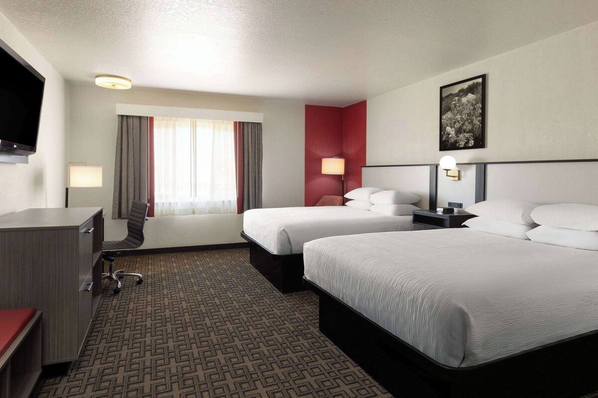 A hotel room with two beds, a desk, a chair, a TV, and a window with curtains.