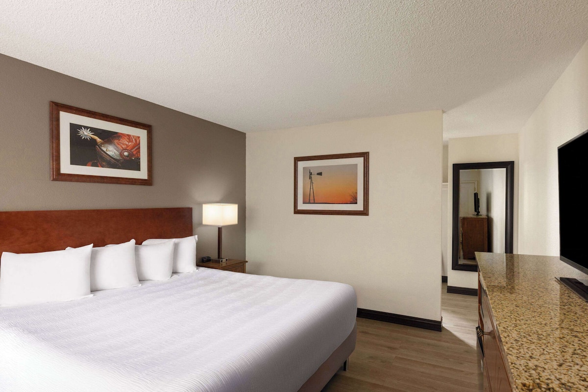 A hotel room with a large bed, a nightstand with a lamp, two framed pictures on the wall, a wooden dresser, and a mirror.