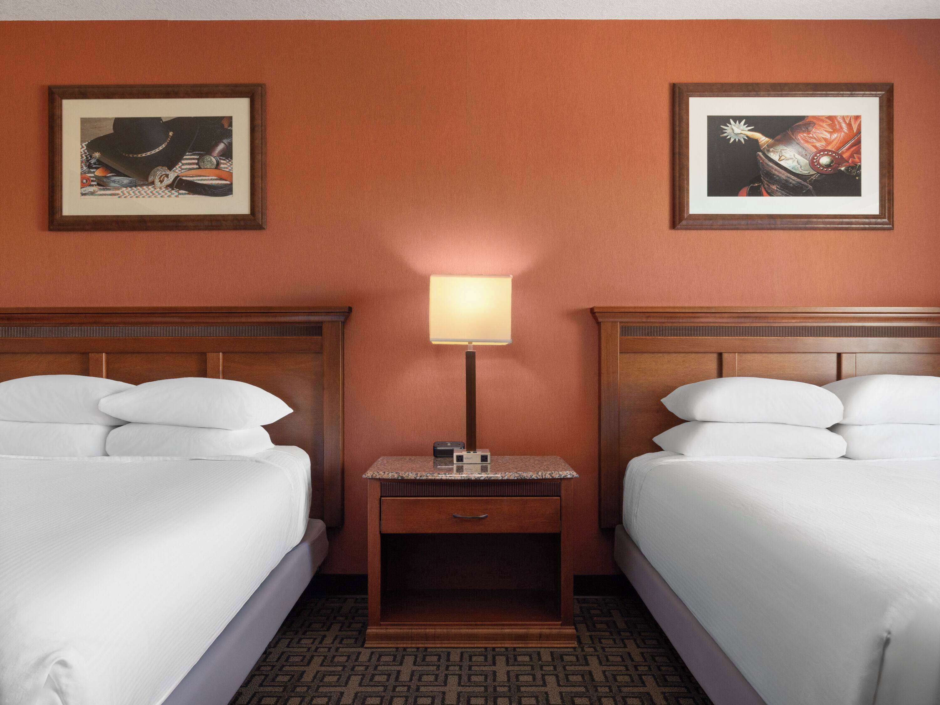 A hotel room with two beds, a nightstand with a lamp, and two framed pictures on the wall.