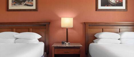 A hotel room with two beds, a nightstand with a lamp, and two framed pictures on the wall.