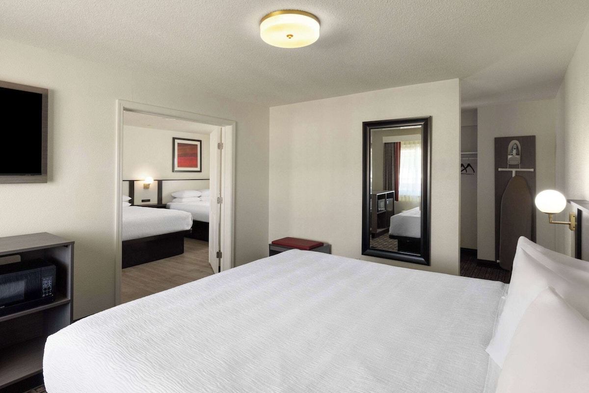 A hotel room with a large bed, a desk with a computer, a mirror, and a wardrobe.