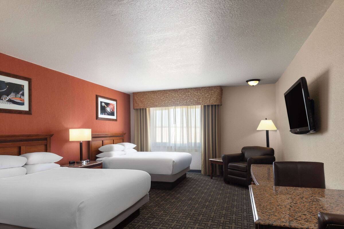 A hotel room with two beds, a desk, a chair, a TV, and a window with curtains.