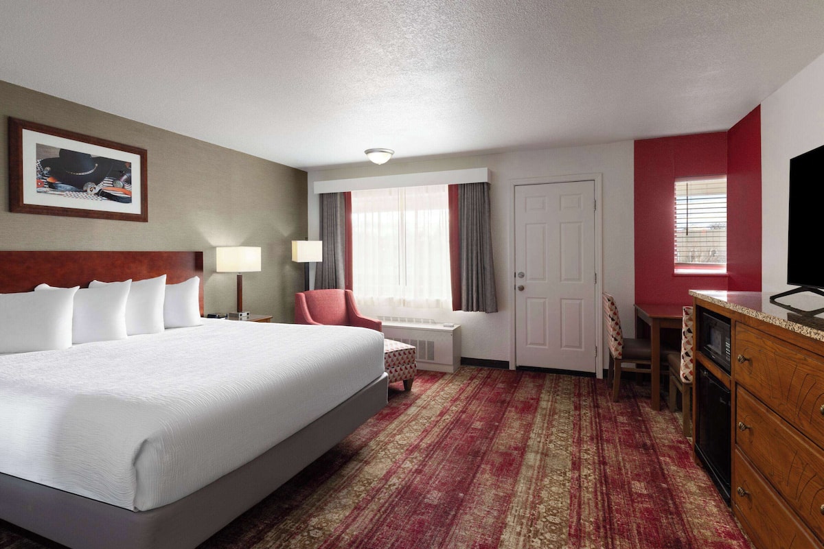 A hotel room with a large bed, a desk, a chair, a television, and a window with curtains.