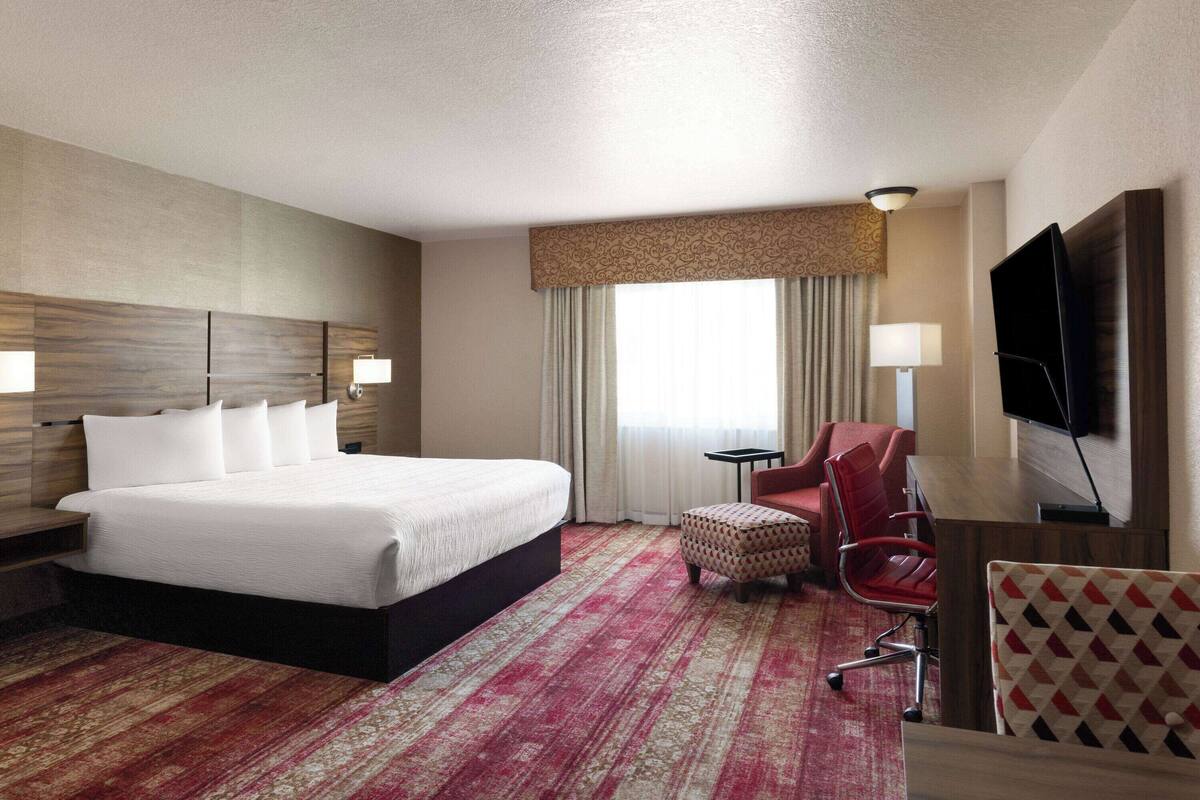 A hotel room with a large bed, a small table, a chair, a TV, and a window with curtains.