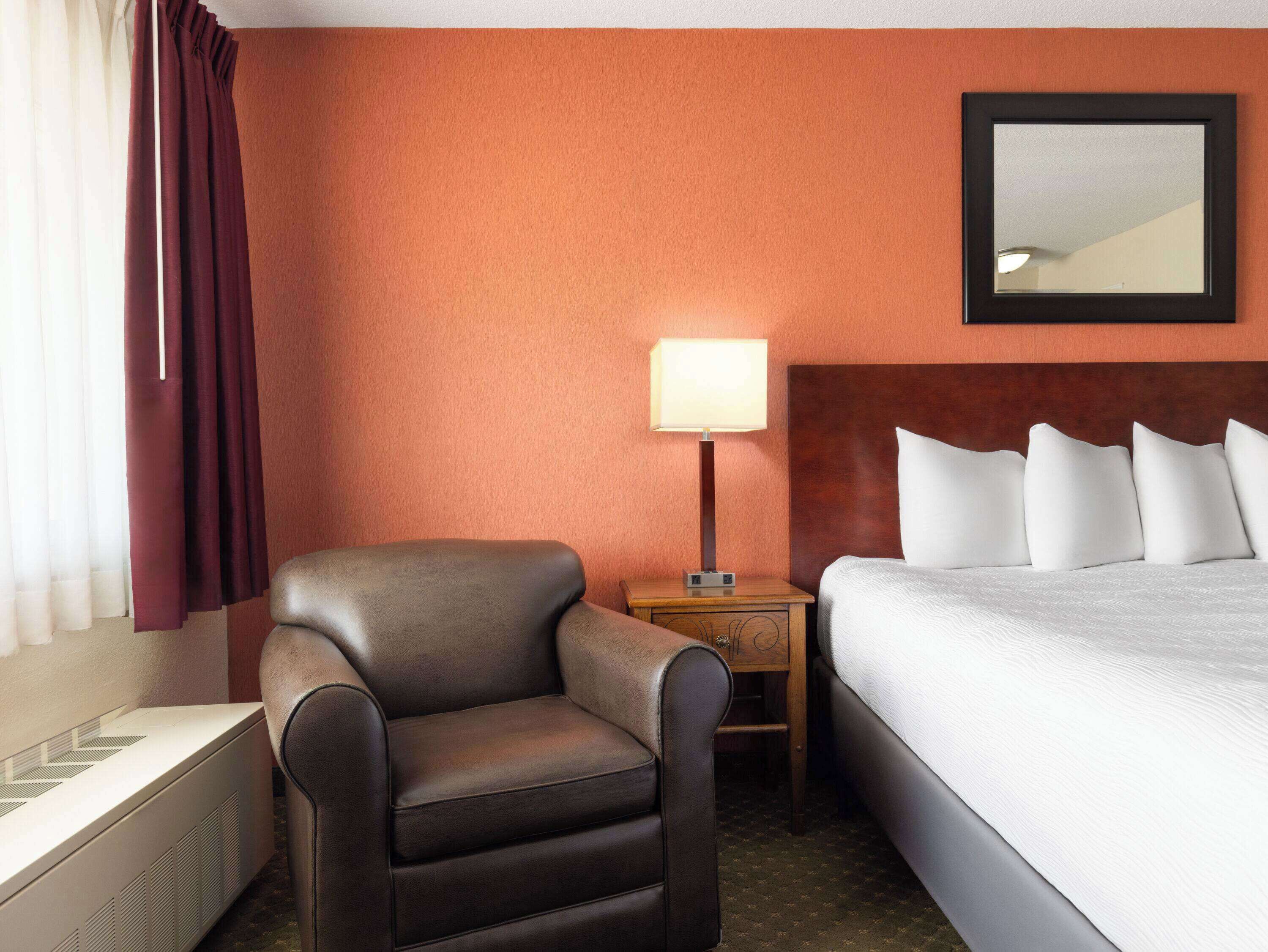Une chambre d’hôtel avec un lit, une chaise, une table de chevet avec une lampe et un radiateur.