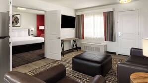 Ein Hotelzimmer mit Bett, Schreibtisch, Fernseher, einer Sitzecke mit Poufs und einem Fenster mit Vorhängen.