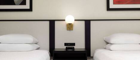 A hotel room with two beds, a nightstand with a lamp, and artwork on the walls.