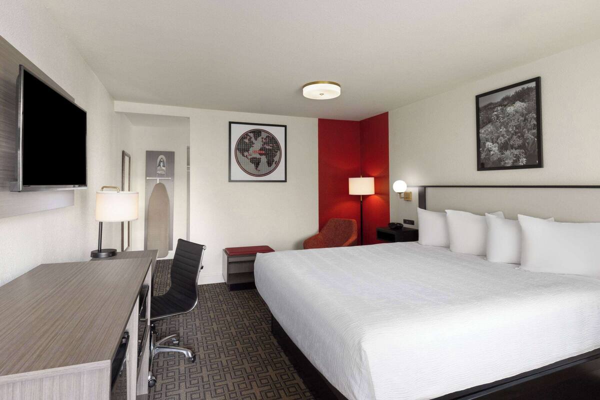 A hotel room with a bed, desk, chair, and a TV.