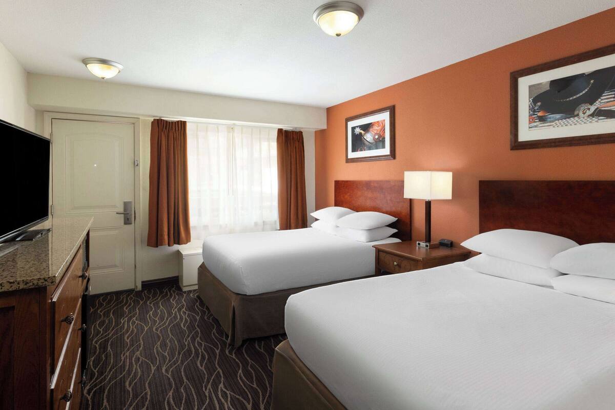 A hotel room with two beds, a desk with a flat-screen TV, a lamp, and a framed picture on the wall.