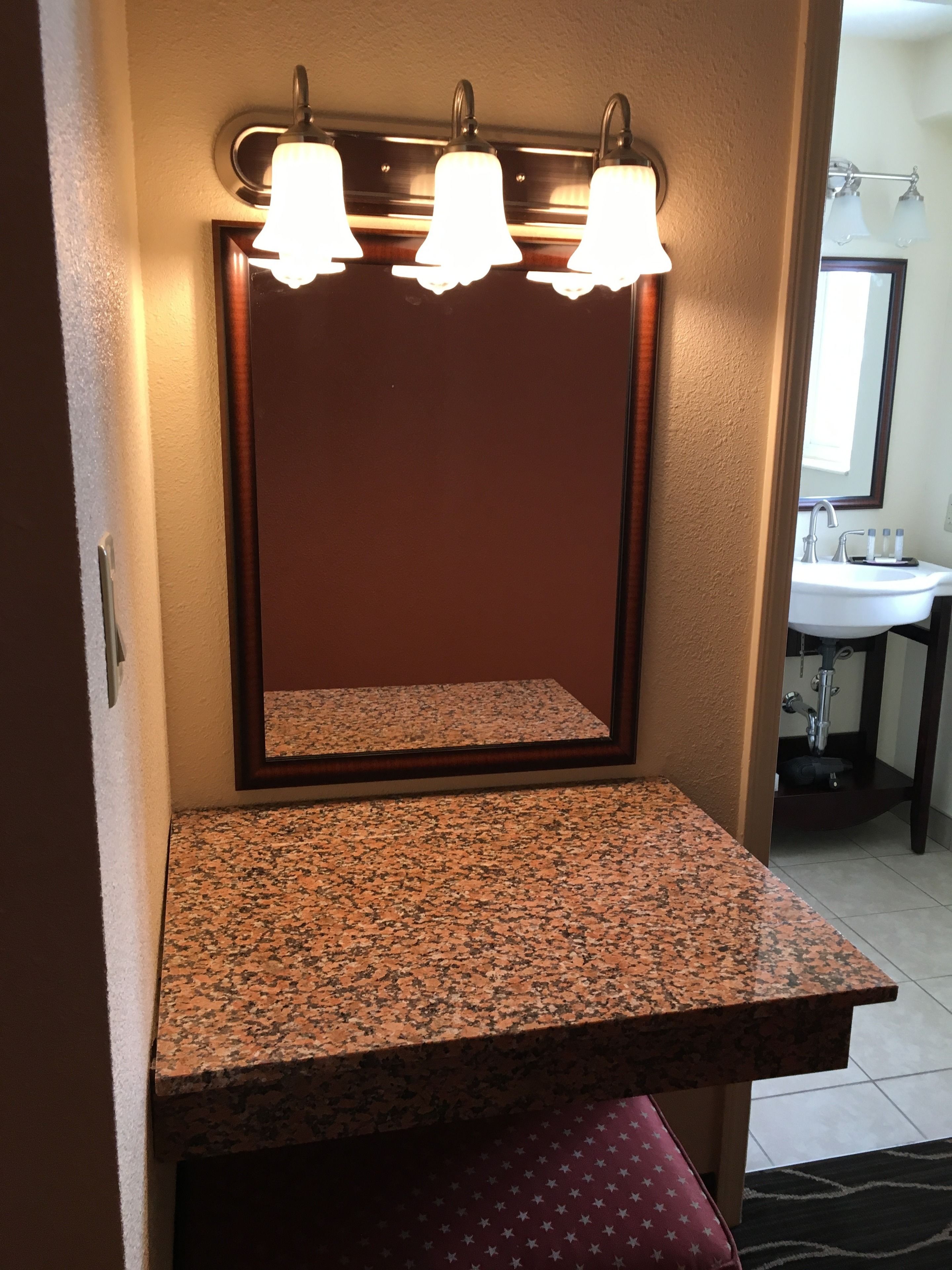 A bathroom vanity with a granite countertop, a mirror above it, and three wall-mounted lights.