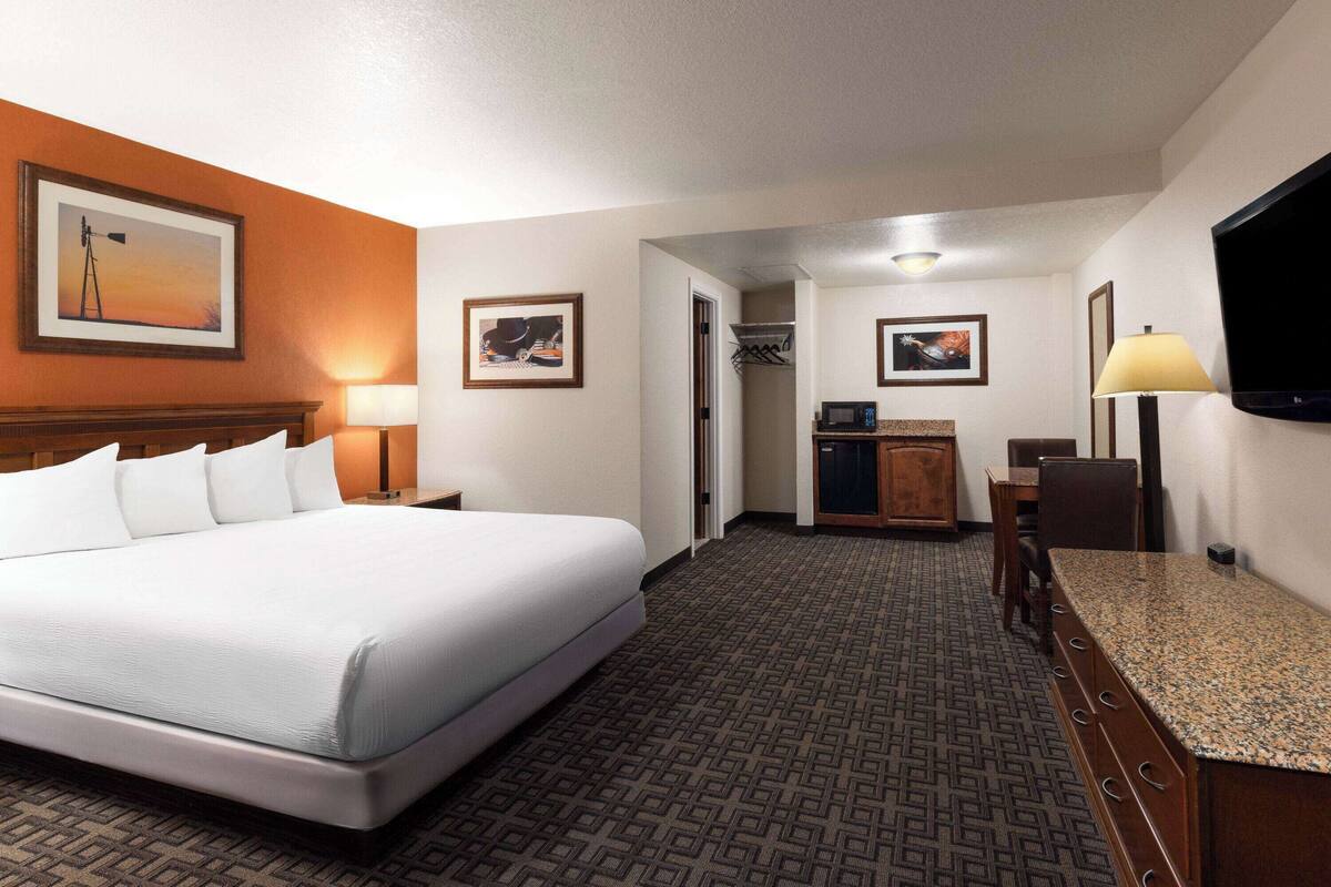 A hotel room with a large bed, a desk with a computer, a TV, and artwork on the walls.