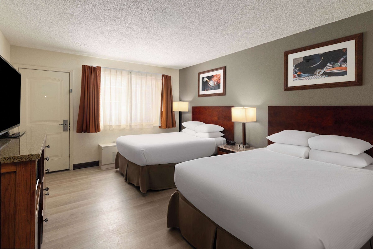 A hotel room with two beds, a television, a desk, and a window with curtains.
