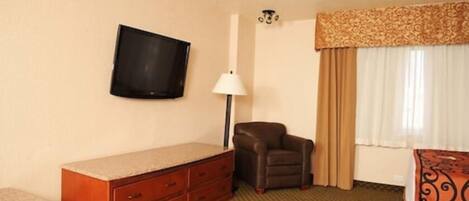 Une chambre d’hôtel dotée d’un téléviseur à écran plat fixé au mur, d’un fauteuil en cuir, d’une commode en bois avec des tiroirs, d’un lampadaire et d’un lit recouvert d’une couvre-lit à motifs.