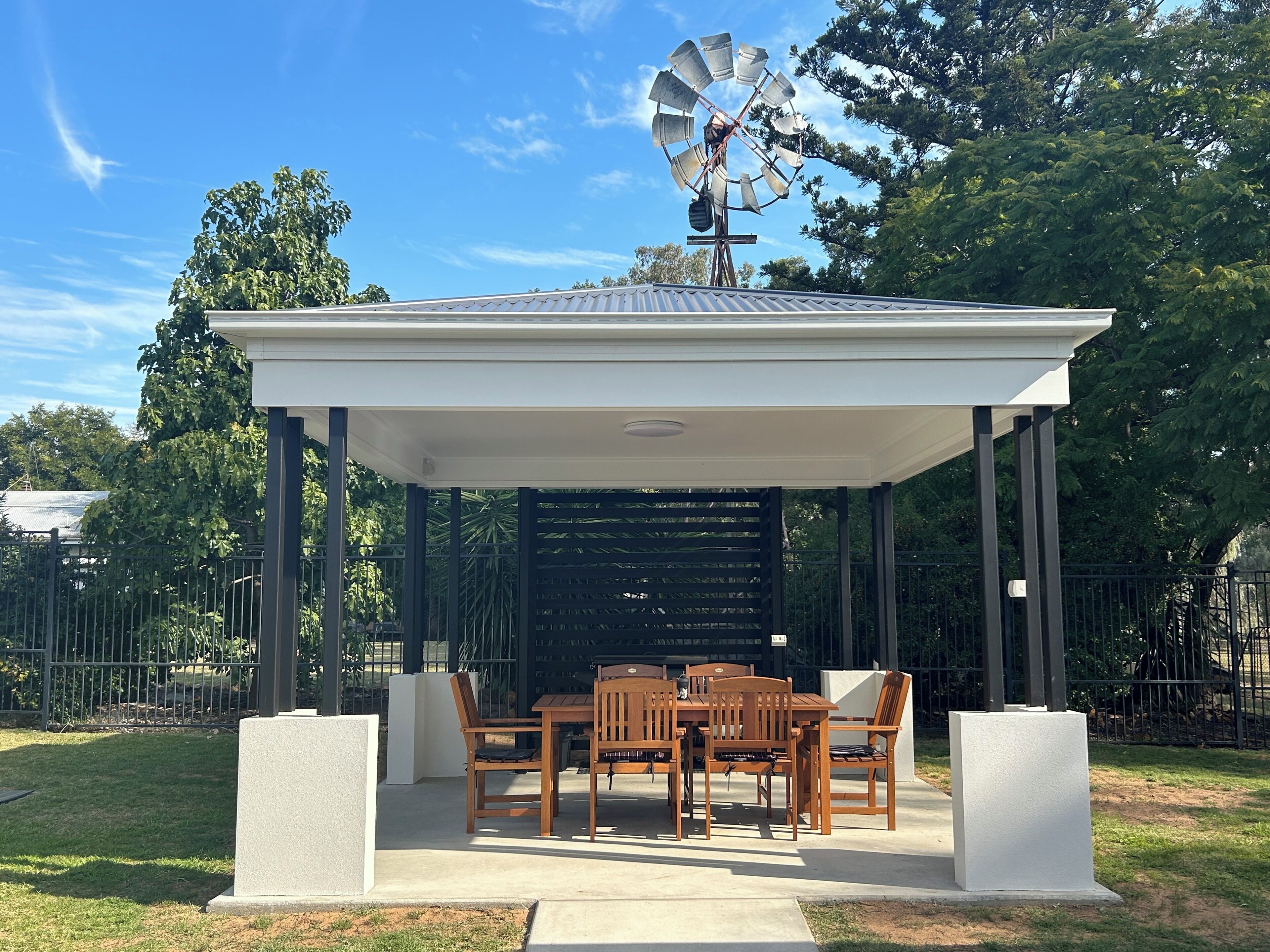 A gazebo with a windmill, wooden table and chairs, and a concrete floor.