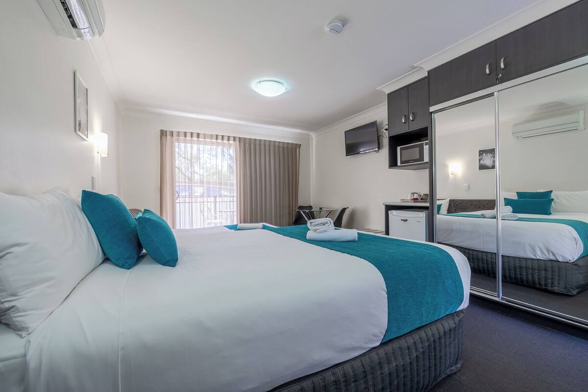 A hotel room with a large bed, a desk, a chair, a TV, and a mirror.