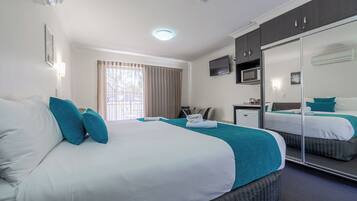 A hotel room with a large bed, a desk, a chair, a TV, and a mirror.