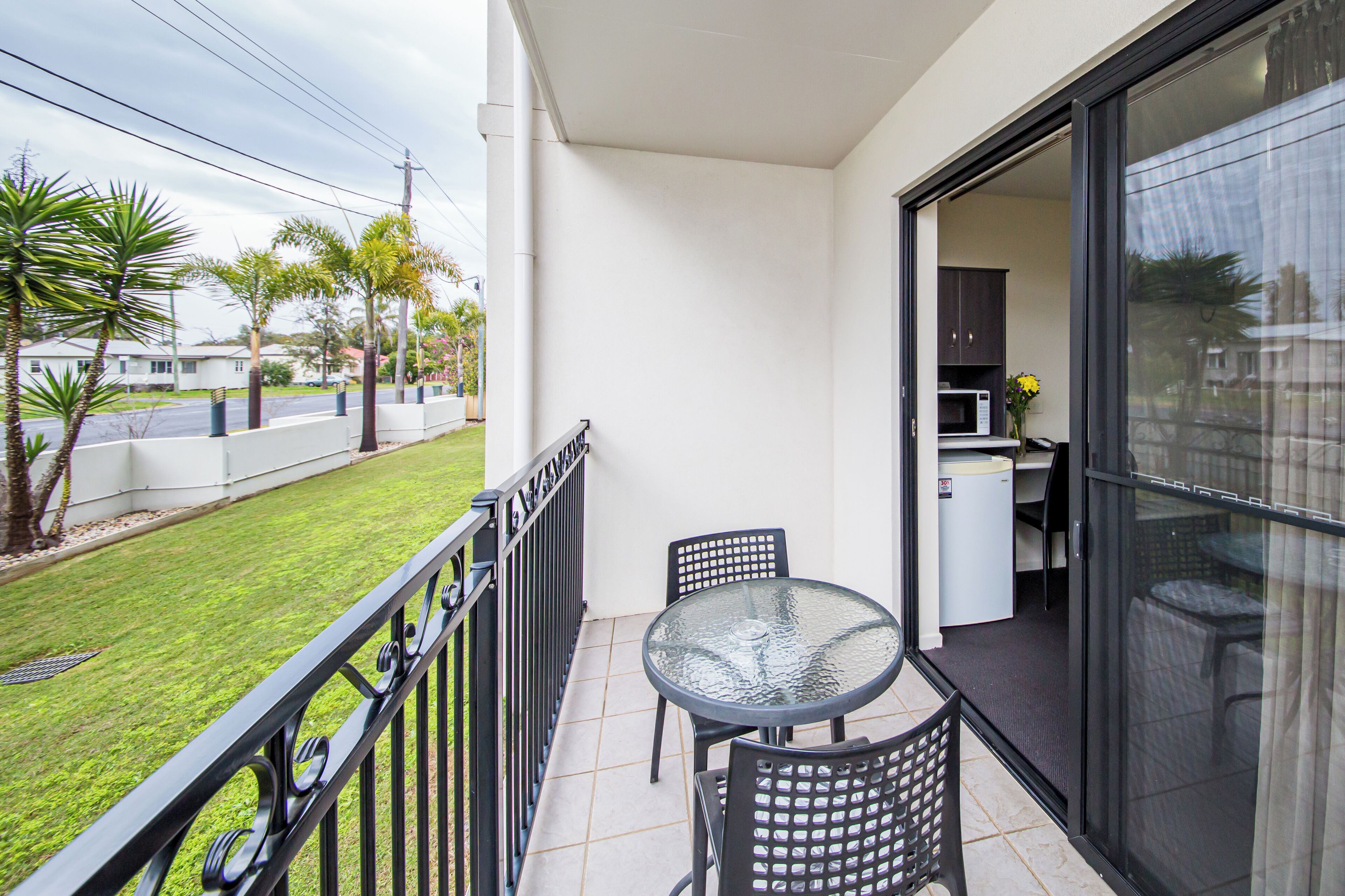 A balcony with a glass table and chairs, a white microwave, and a small kitchen area.