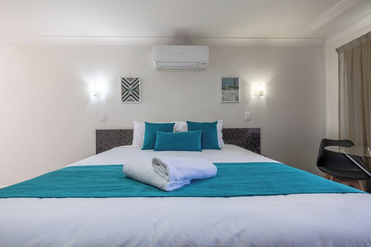 A hotel room with a bed, a wall-mounted air conditioner, and two wall-mounted light fixtures.