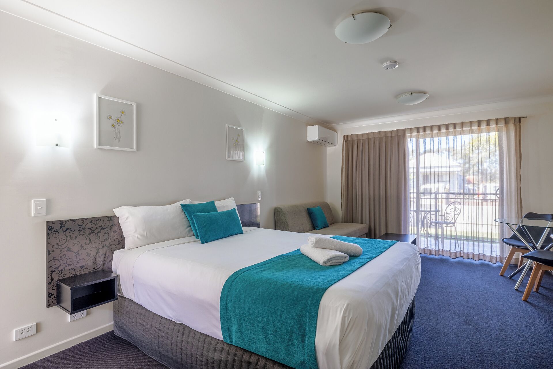 A hotel room with a bed, a sofa, a desk, and a balcony with curtains.