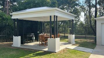 A covered patio area with a table and chairs, surrounded by a fence and trees.