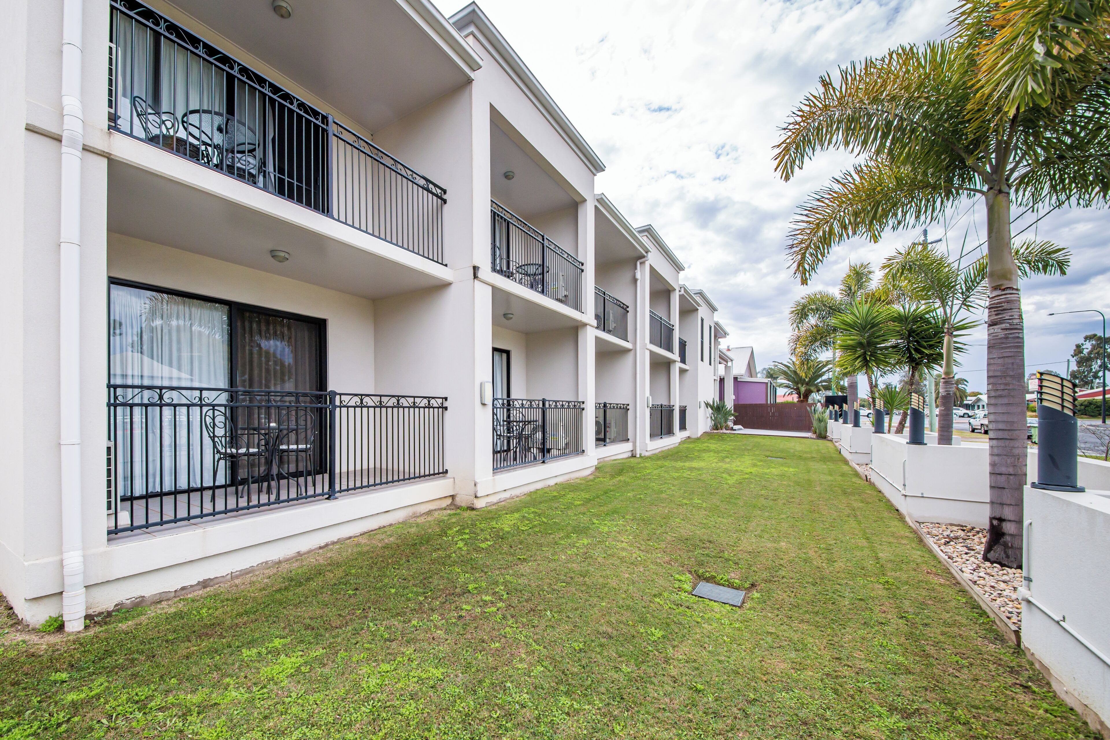 Un hotel de varios pisos con balcones, un césped bien cuidado y palmeras.