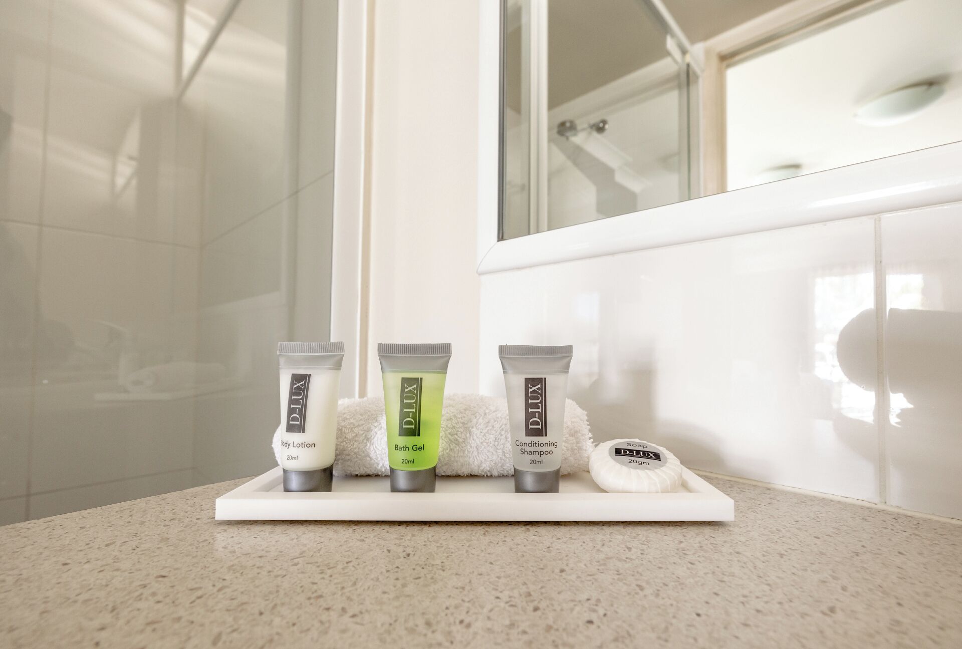 Un meuble de salle de bain sur lequel sont disposés trois produits de la gamme D-Lux pour le soin de la peau : une lotion pour le corps, un gel de bain et un shampooing après-shampooing.
