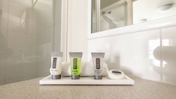 Un meuble de salle de bain sur lequel sont disposés trois produits de la gamme D-Lux pour le soin de la peau : une lotion pour le corps, un gel de bain et un shampooing après-shampooing.