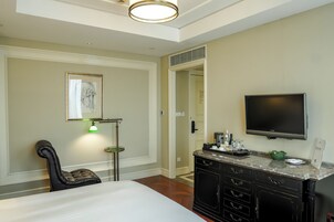 A hotel room with a bed, a desk, a TV, and a minibar.