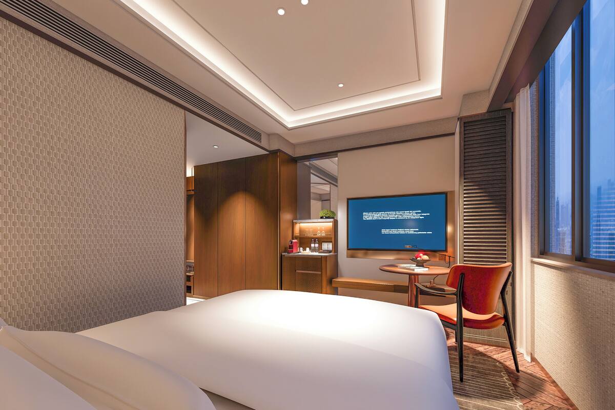 A modern hotel room with a large bed, a desk with a chair, a television, and a window with blinds.