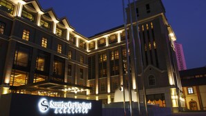A multi-story hotel with a prominent entrance and illuminated signage. - Sunrise on the Bund (Shanghai)