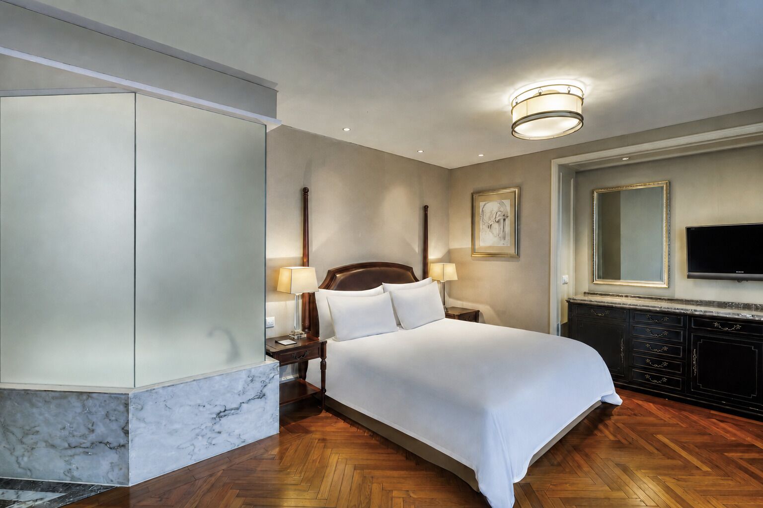 Een hotelkamer met een groot bed, een televisie, een marmeren accentmuur en een houten vloer.