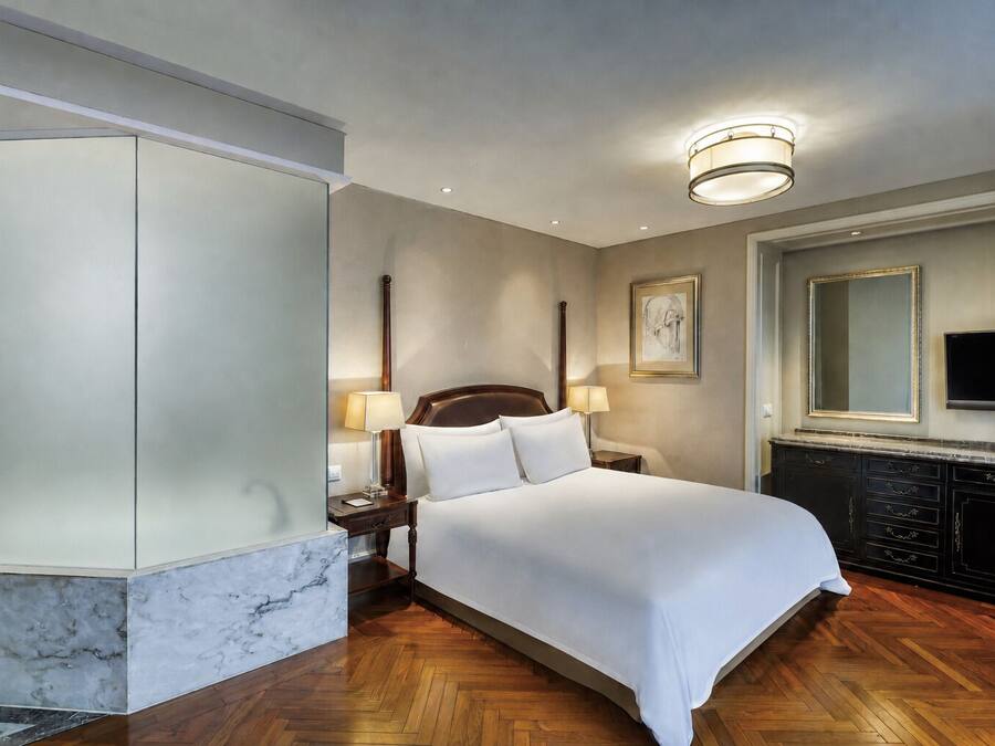 Een hotelkamer met een groot bed, een televisie, een marmeren accentmuur en een houten vloer.